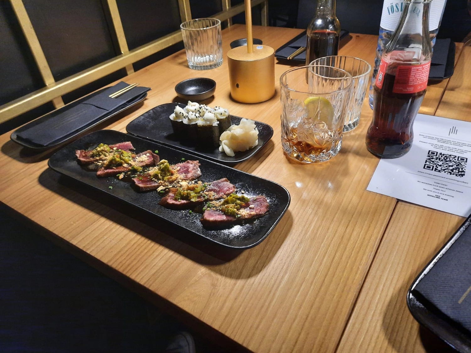Mbaye Jeng – Companionship Service - Das Bild zeigt eine Mahlzeit aus Sushi und gebratenem Rindfleisch auf einem Holztisch, wahrscheinlich in einem japanischen Restaurant.
