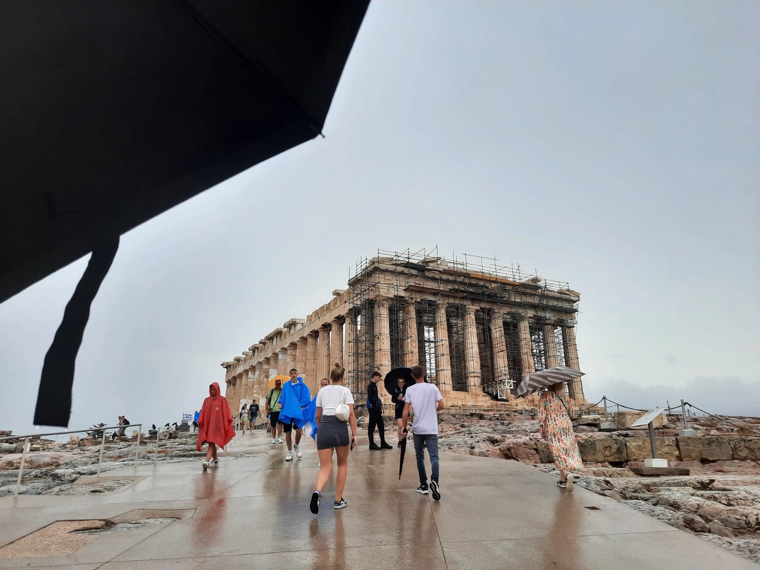 Mbaye Jeng – Companionship Service - Dieses Bild zeigt Besucher, die an einem regnerischen Tag am Parthenon navigieren, einem ikonischen antiken Tempel auf der Akropolis von Athen in Griechenland.