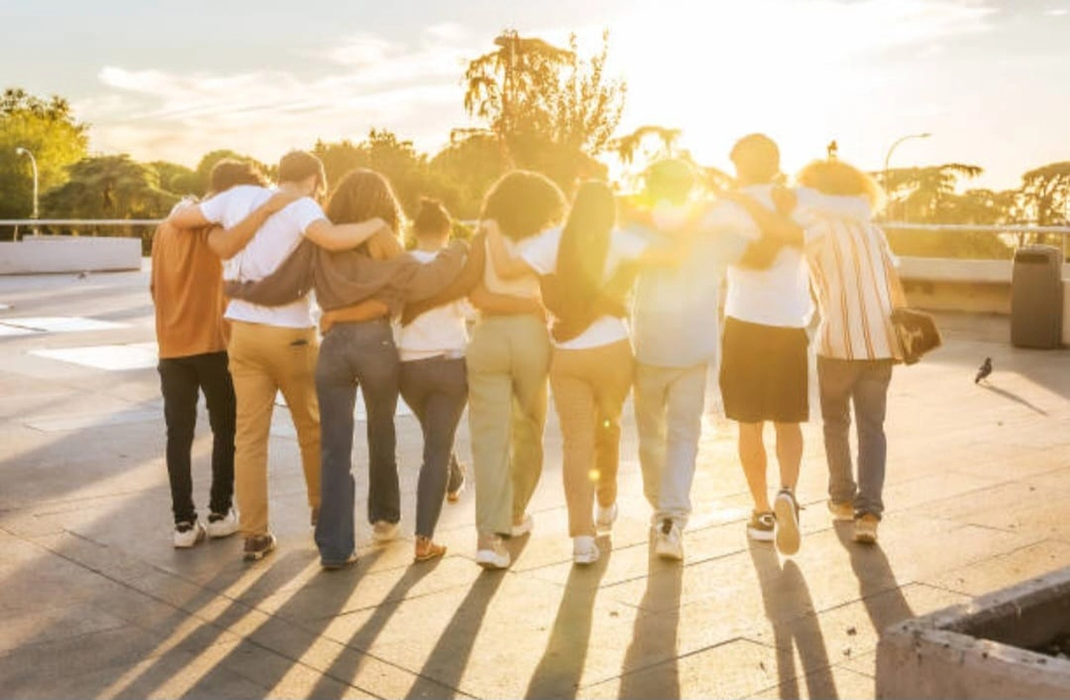 Mbaye Jeng – Companionship Service -Dieses Bild zeigt eine Gruppe von Schülern, die Arm in Arm auf einer Dachterrasse im Sonnenuntergang spazieren gehen.